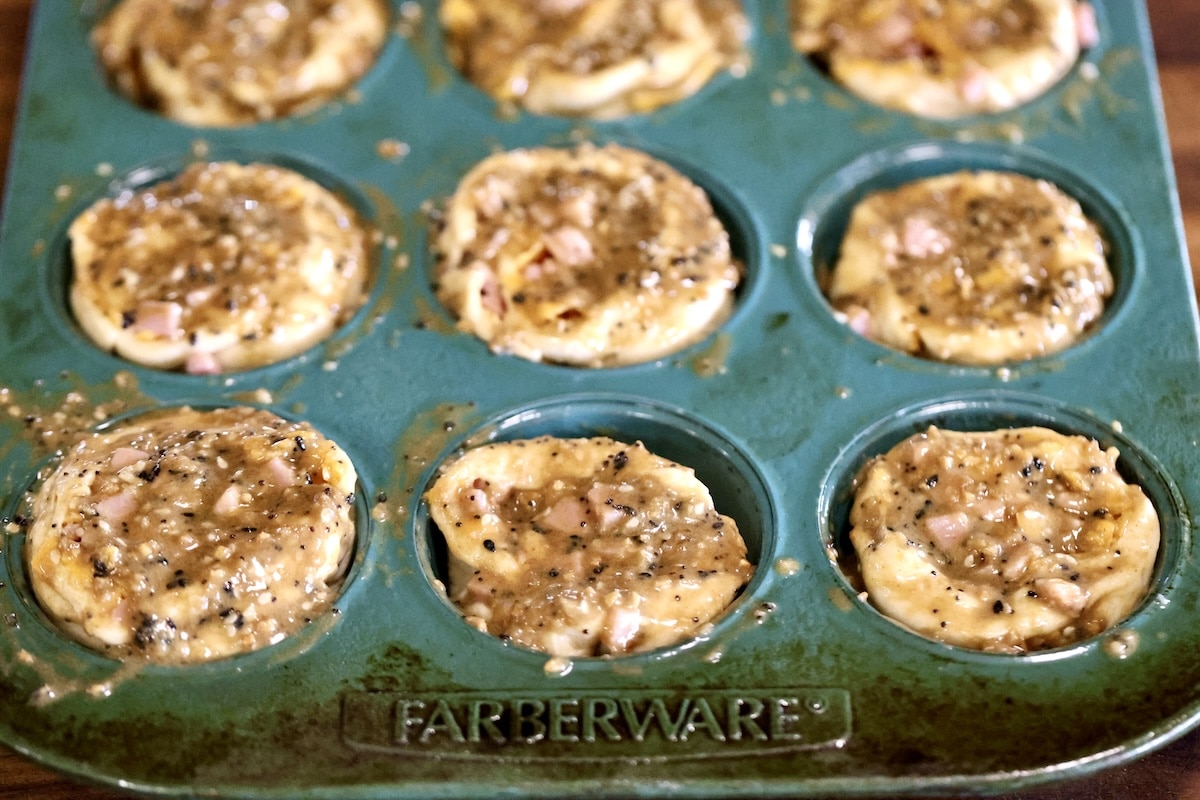 Ham and cheese cruffins in a tin brushed with butter and seasonings.