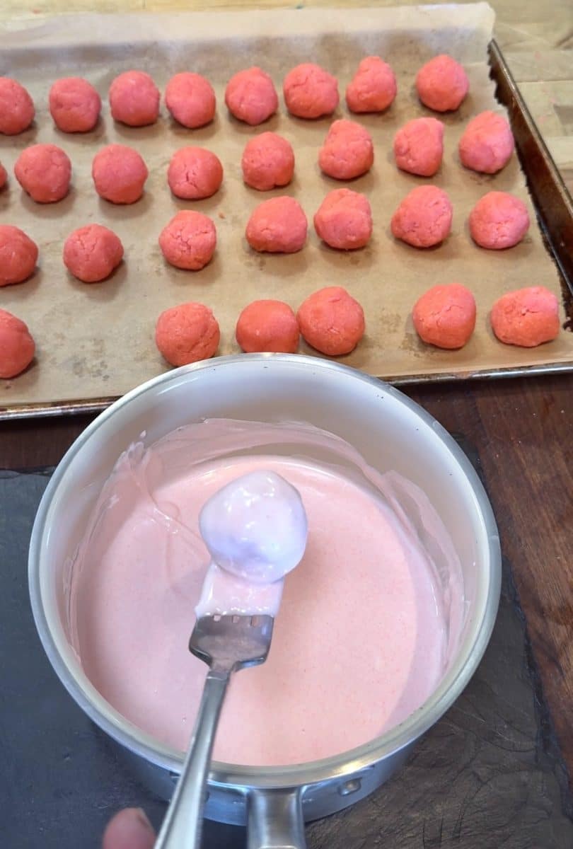 Dipping strawberry cake balls in pink candy coating with a fork.