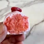 Strawberry cake ball with inside showing, held by hand.