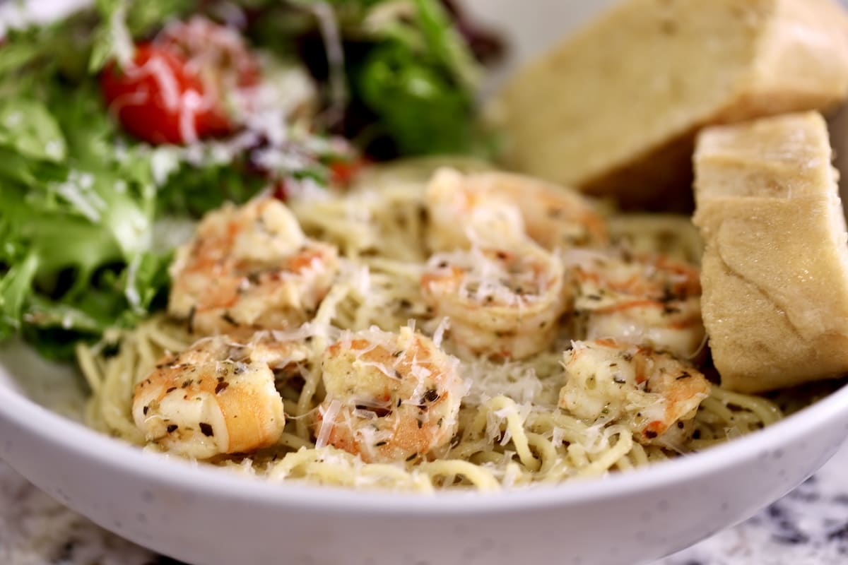 Bowl of shrimp pasta with salad and bread. Bowl of spaghetti topped with shrimp, salad and bread.