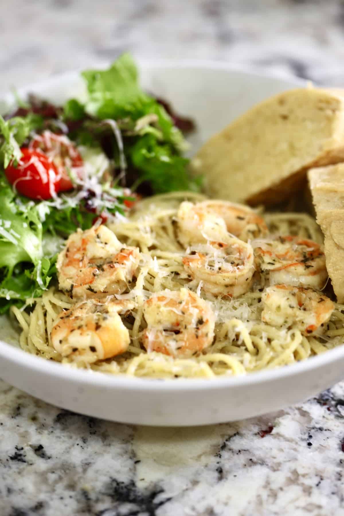 Bowl of Italian shrimp pasta, salad and baguette slices.