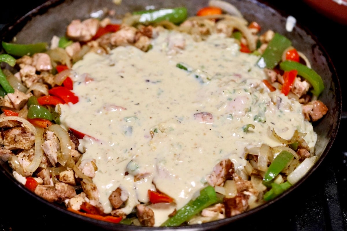 Adding white queso to skillet with chicken fajita mixture.