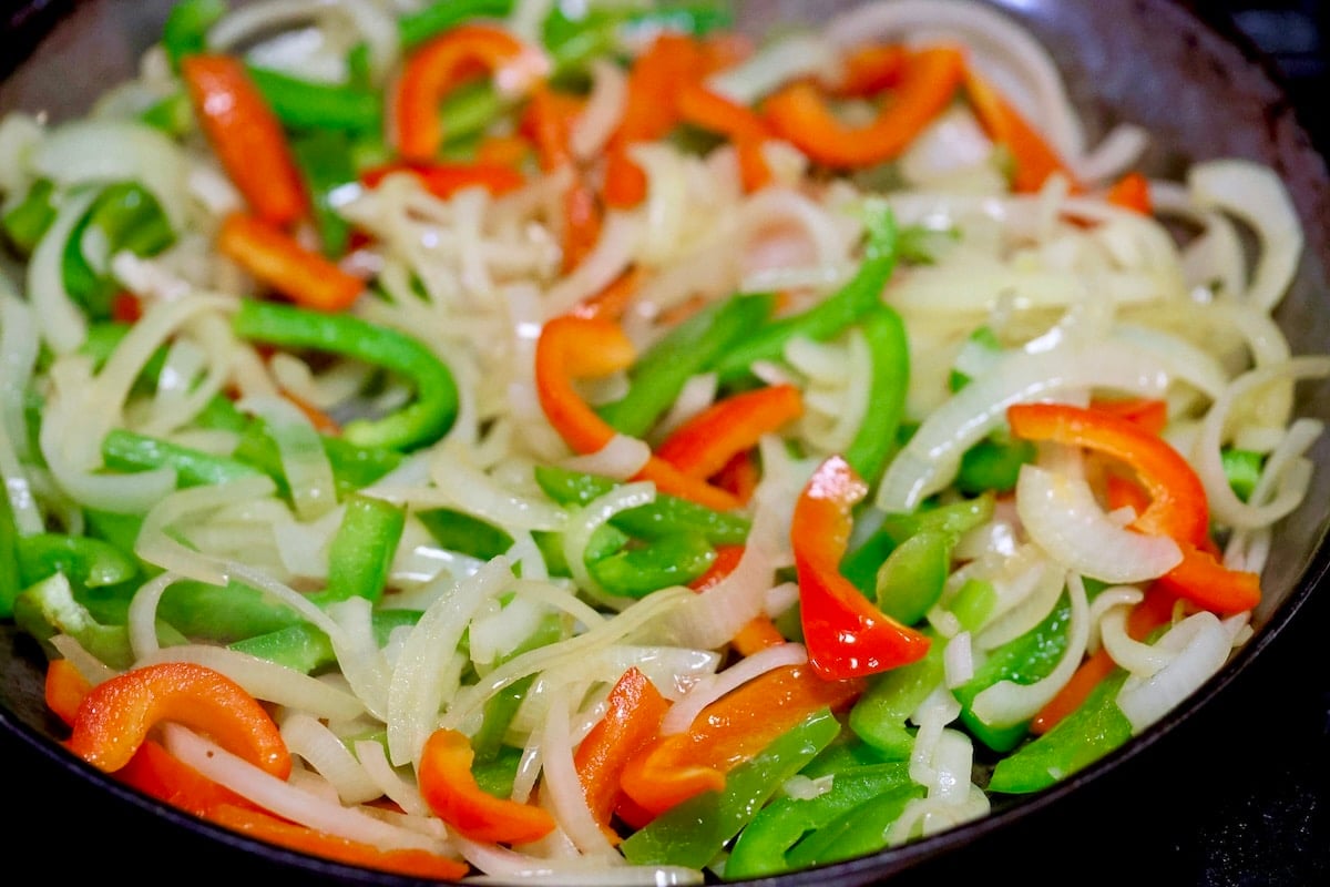 Saut&eacute;ing peppers and onions in a skillet.