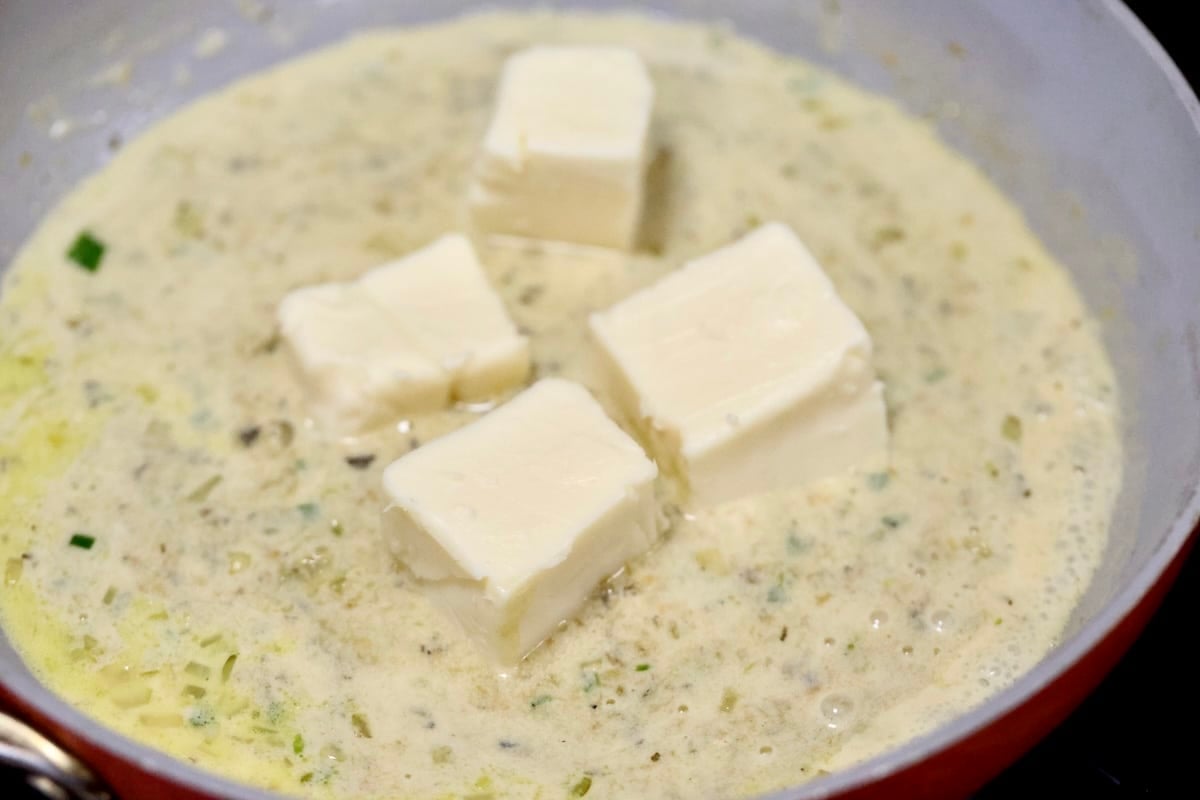 Adding white velveeta making queso in a pan.