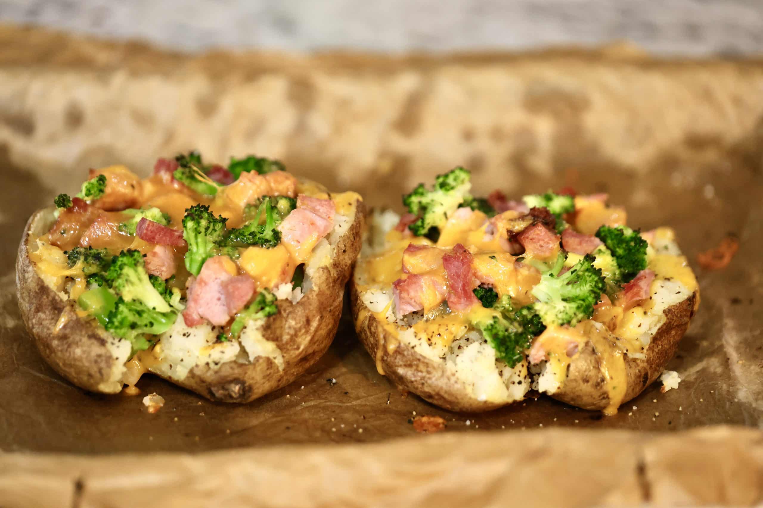 2 ham, broccoli and cheese stuffed baked potatoes on a parchment lined baking sheet.