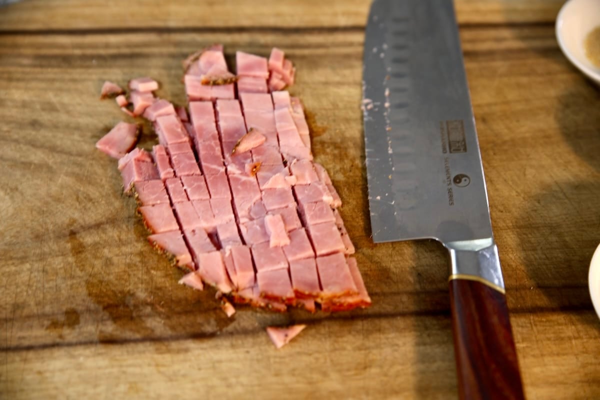 Chopped ham with a knife on a cutting board.