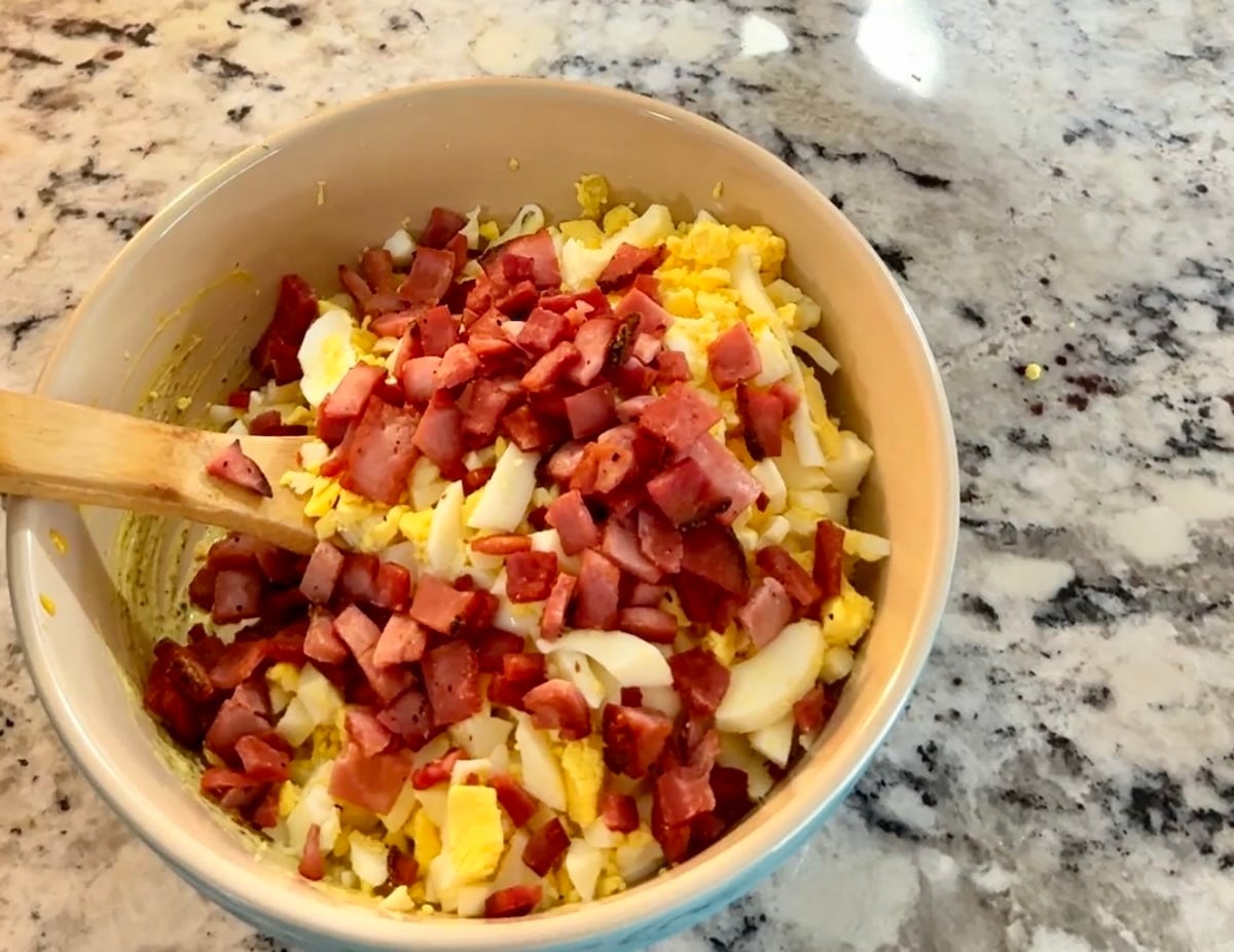 Egg salad with ham in a bowl with wood spoon.