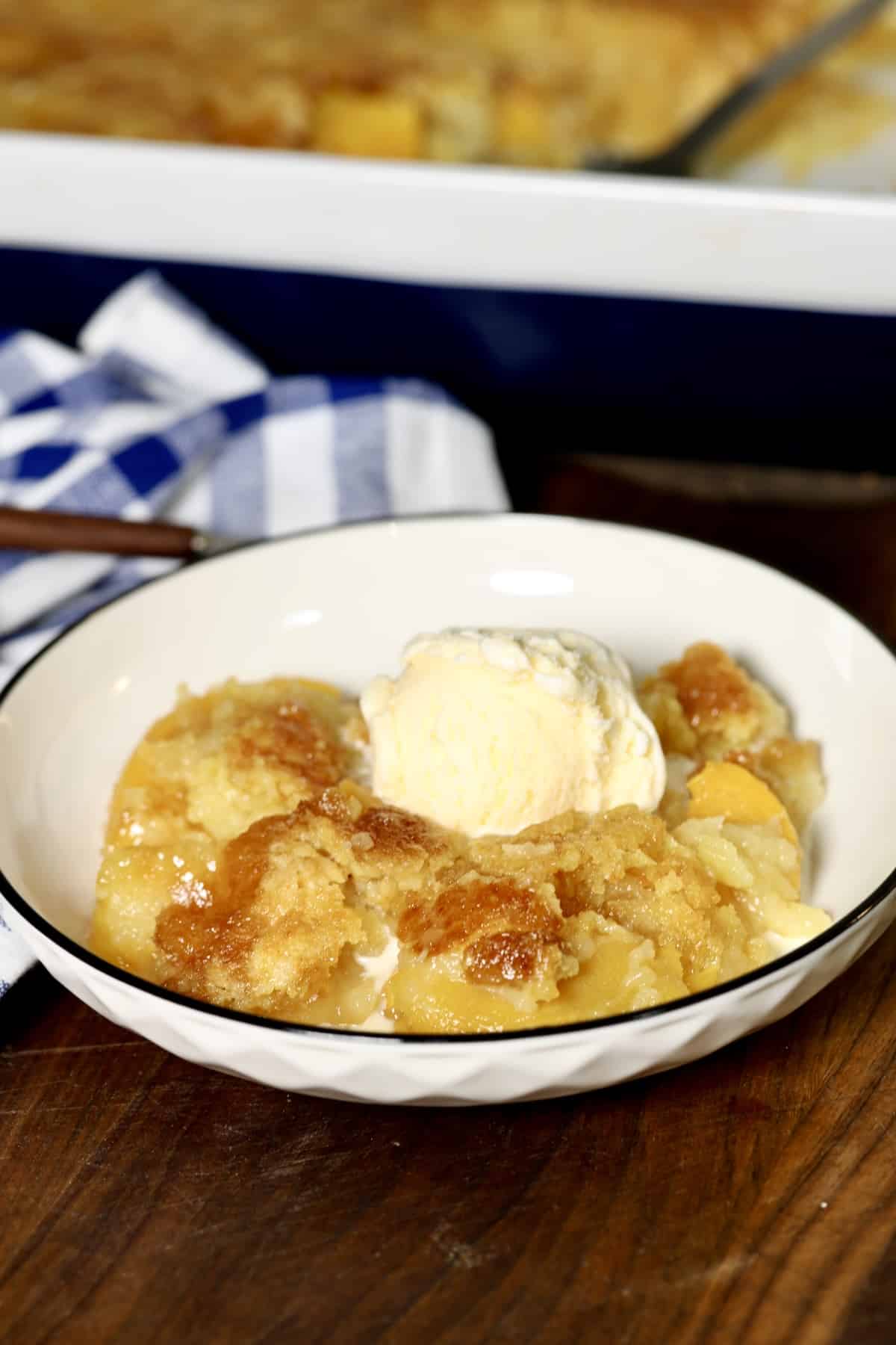 Pineapple peach dump cake recipe. Bowl of pineapple peach dump cake with vanilla ice cream.