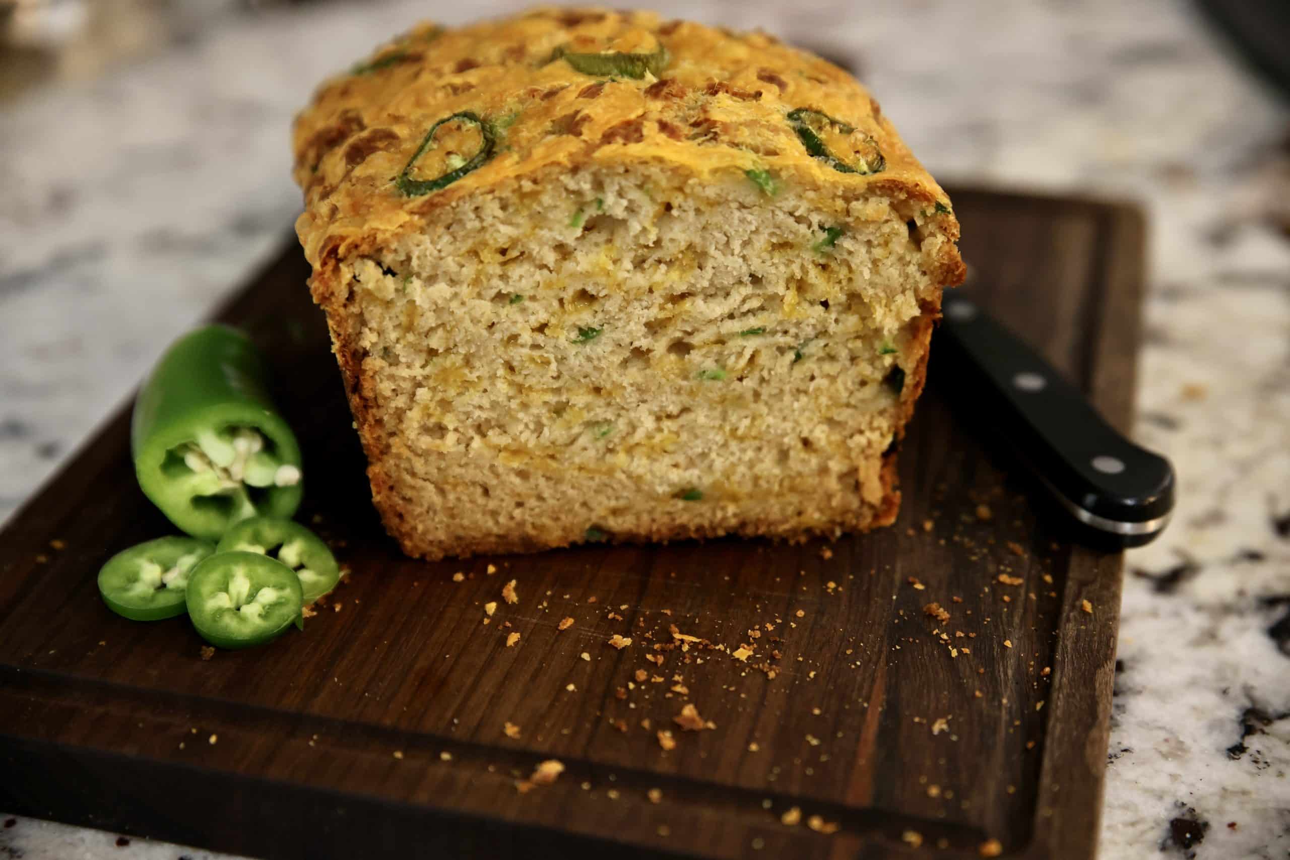 Jalapeno cheddar beer bread loaf, cut so inside showing on a cutting board with jalapeno slices.