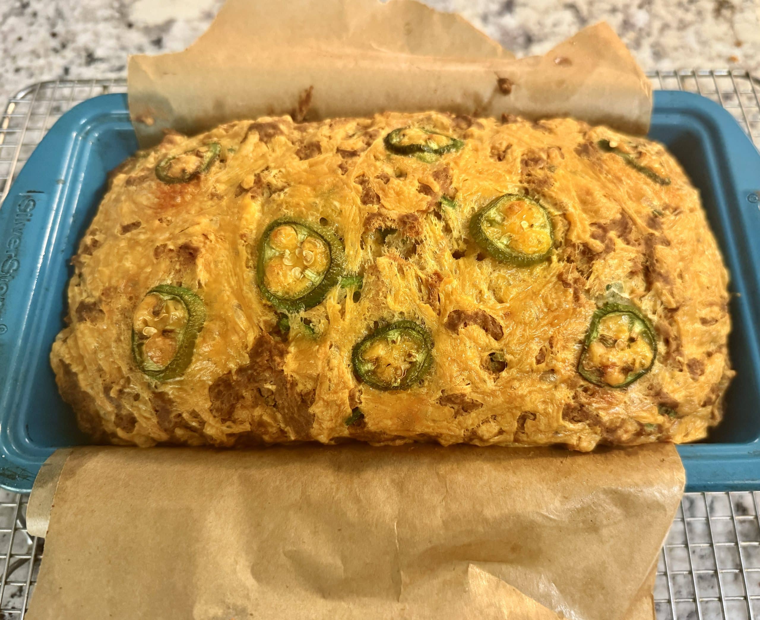 Baked loaf of jalapeno cheddar beer bread in a parchment lined bread pan.