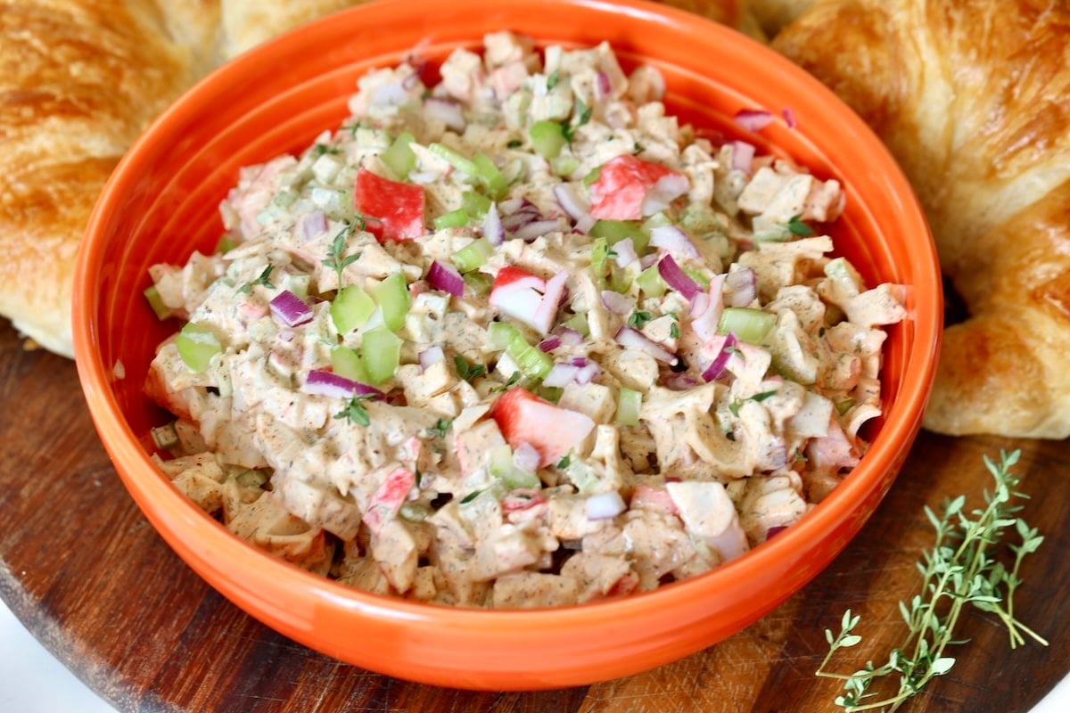 Seafood salad with imitation crab, celery and red onion in an orange bowl with croissants. 